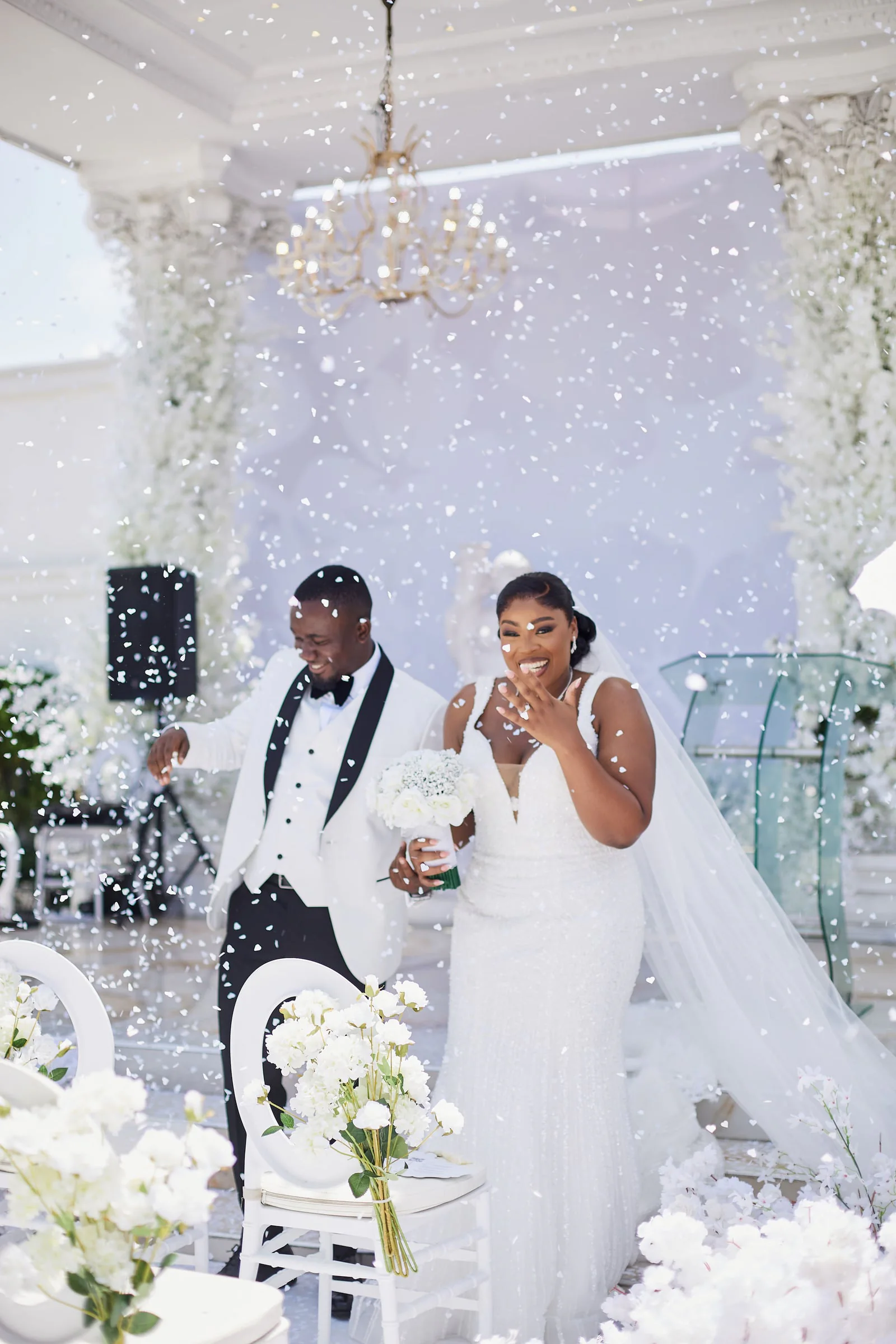 Bride and groom laughing under a shower of confetti beneath a chandelier