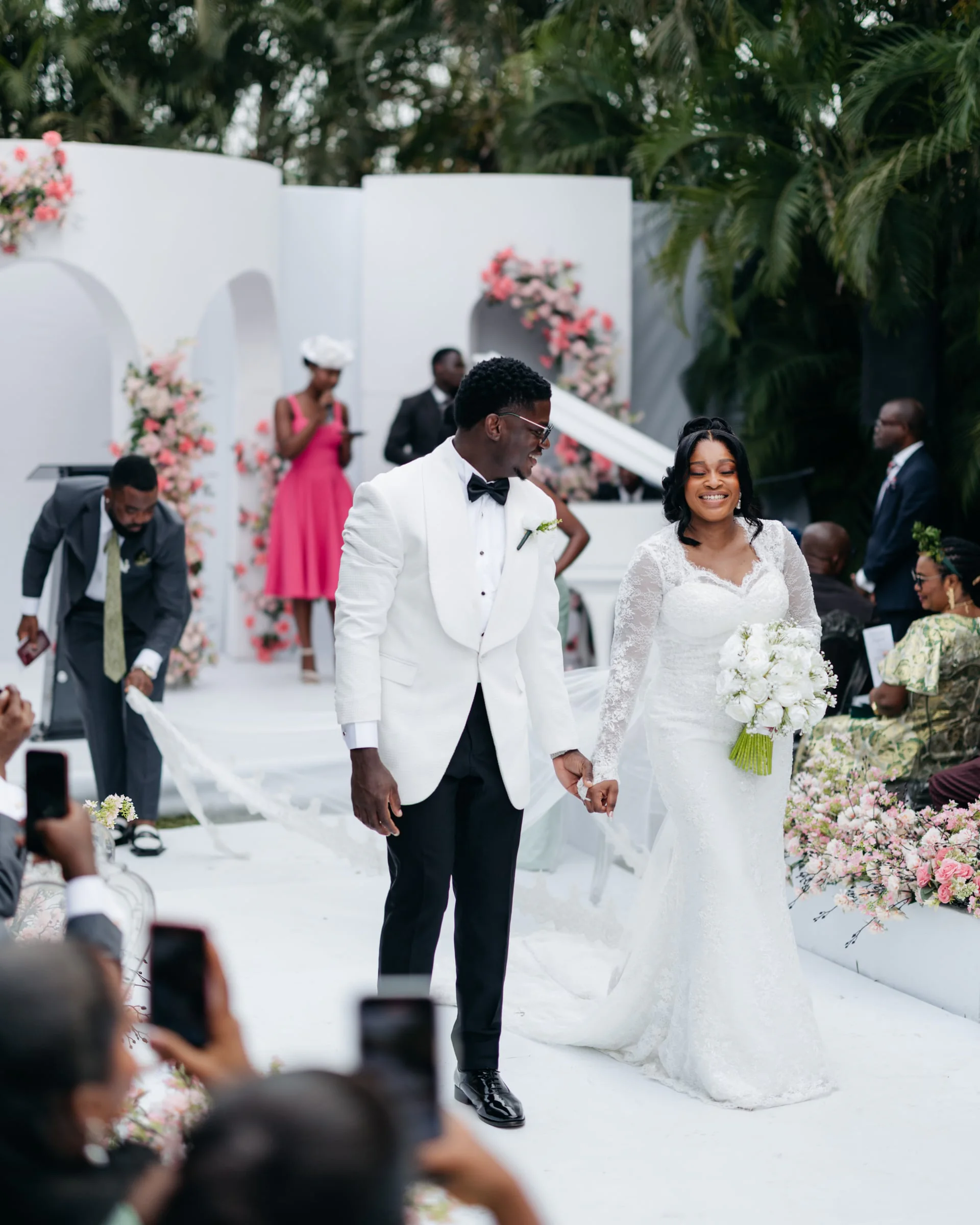 Bride and groom holding hands beneath a floral arch, palm trees behind them