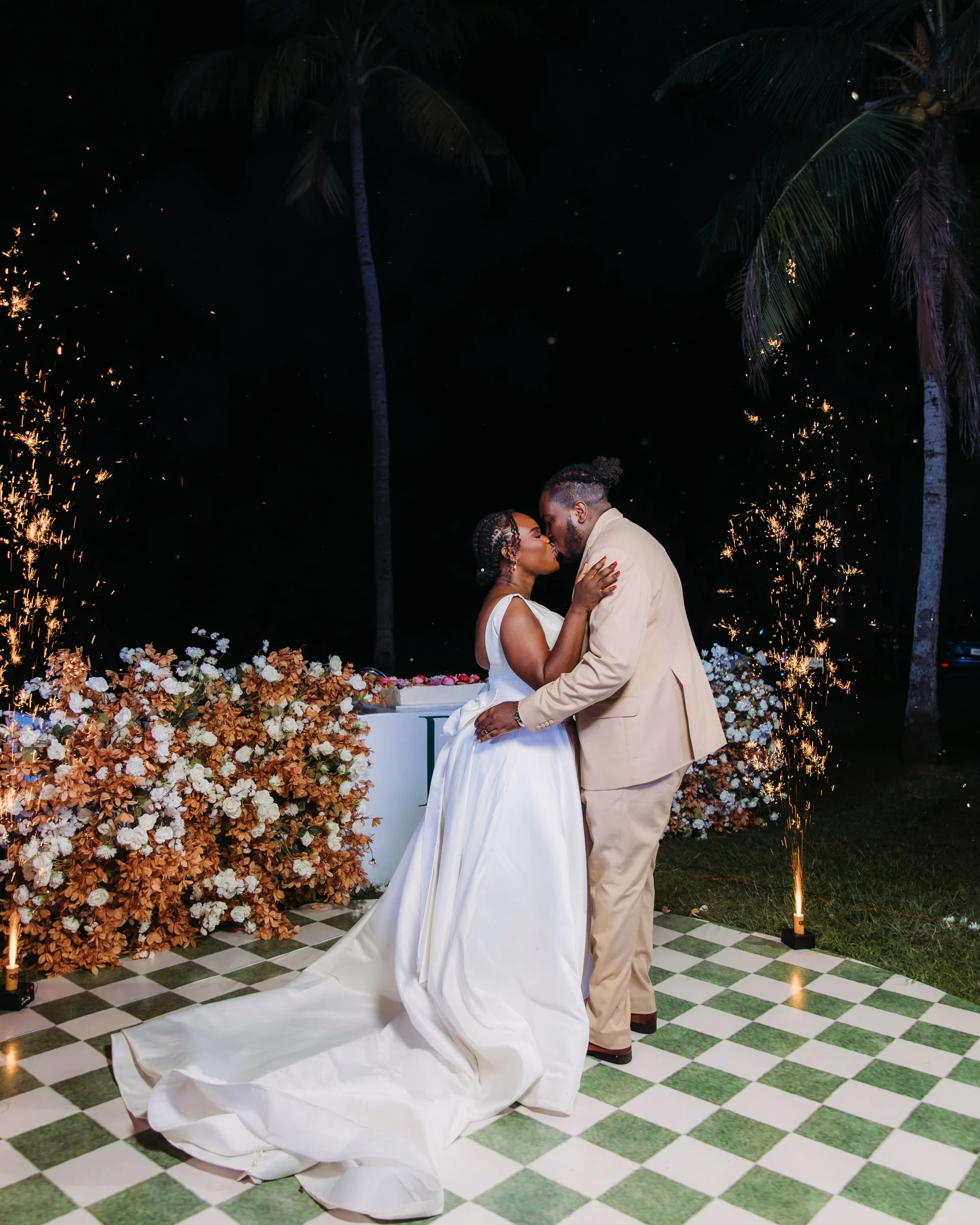 Bride and groom kissing beneath sparklers on a checkered dance floor at night