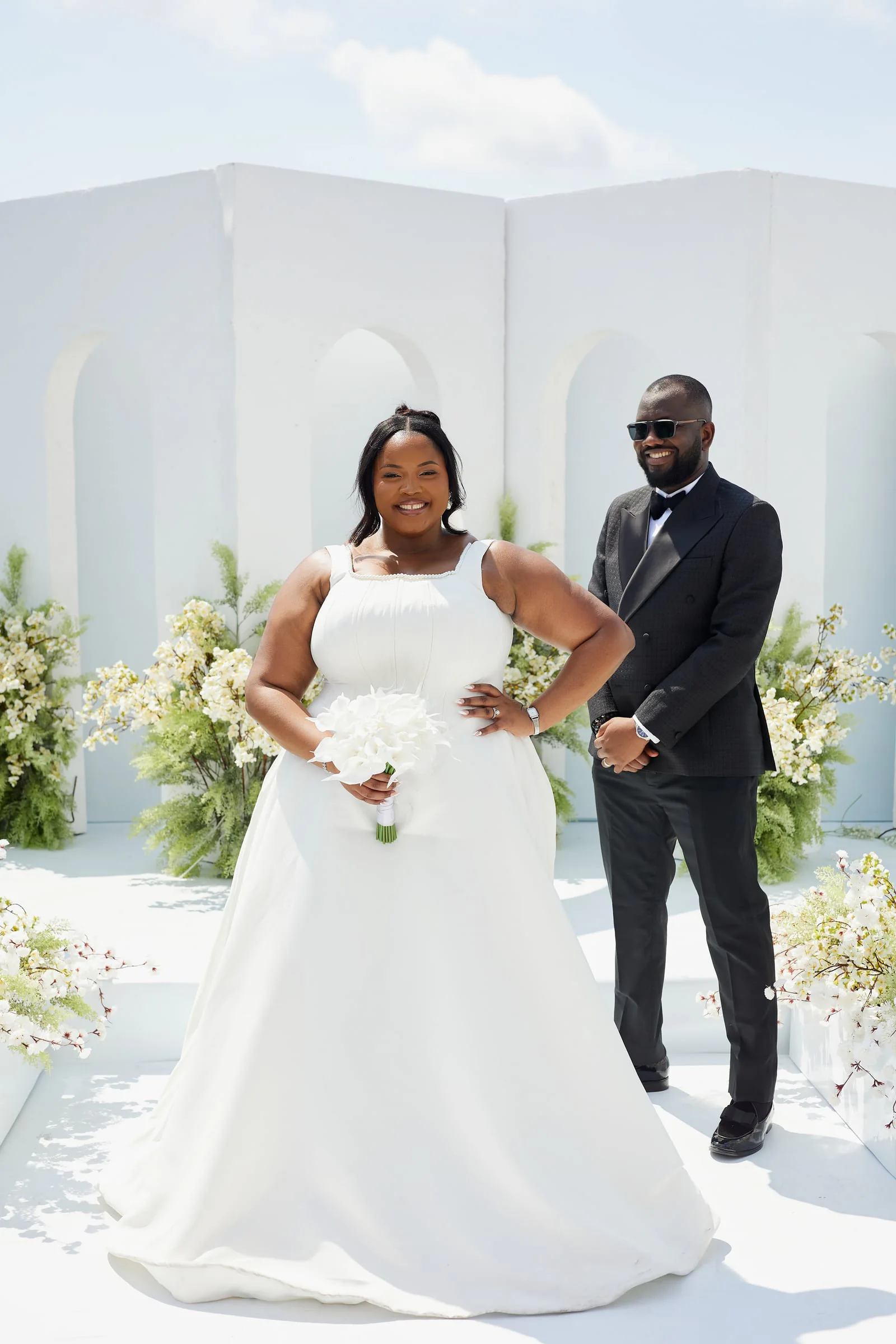 Bride and groom posing before a white arched backdrop with white blossoms