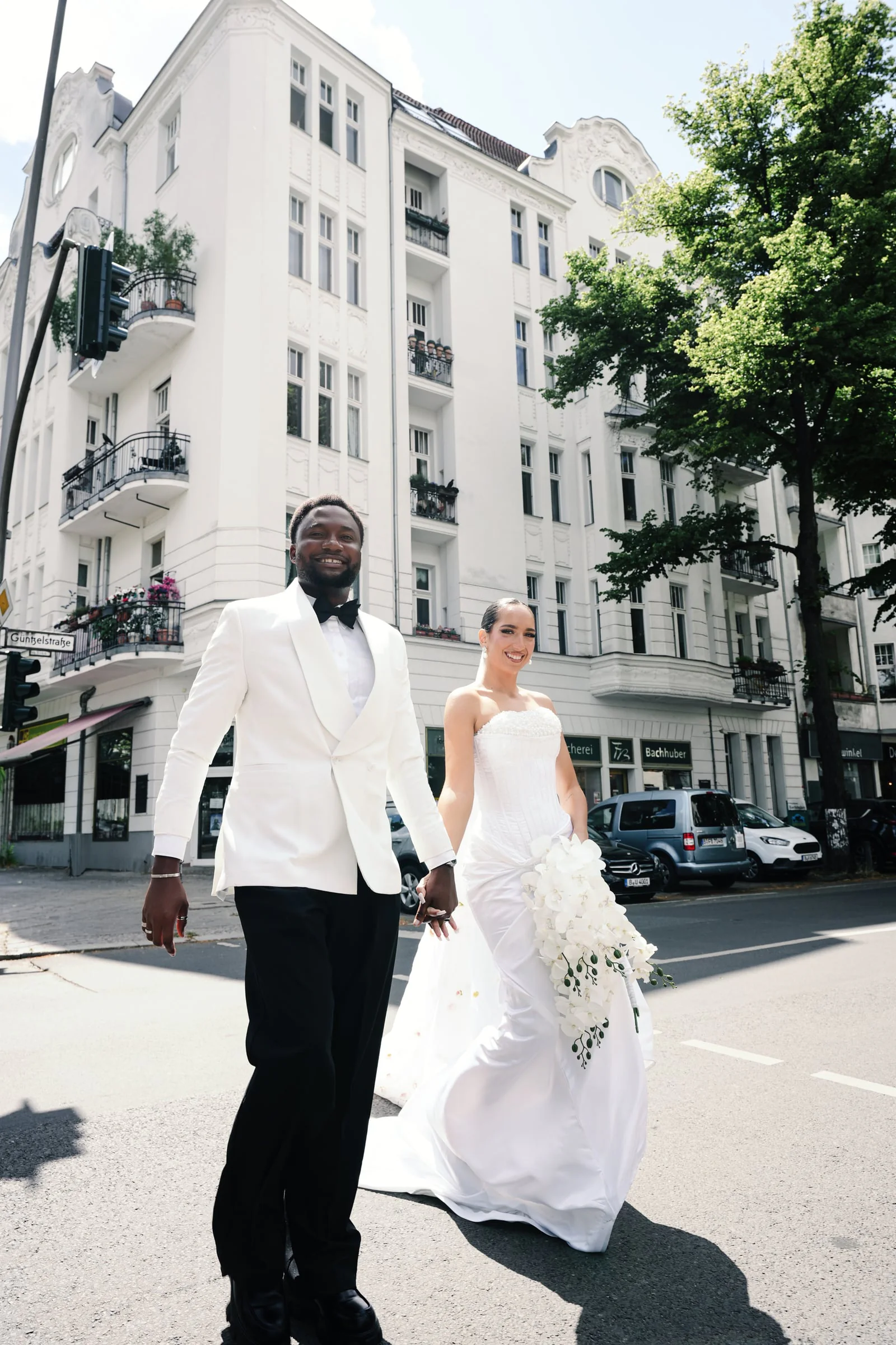Bride and groom holding hands on a city street lined with ornate apartment buildings