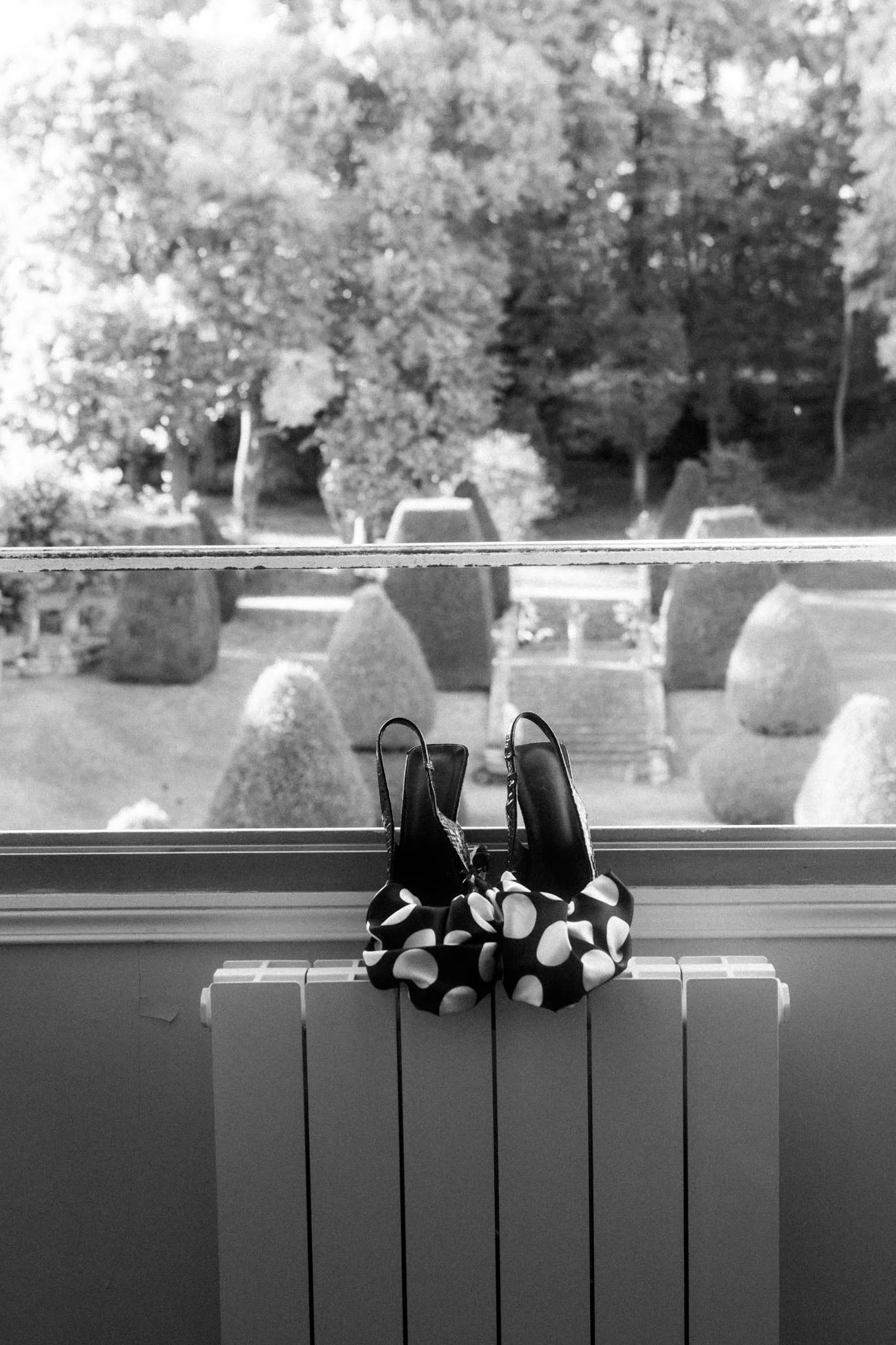 Bridal shoes and a polka-dot bow resting on a windowsill overlooking manicured topiary