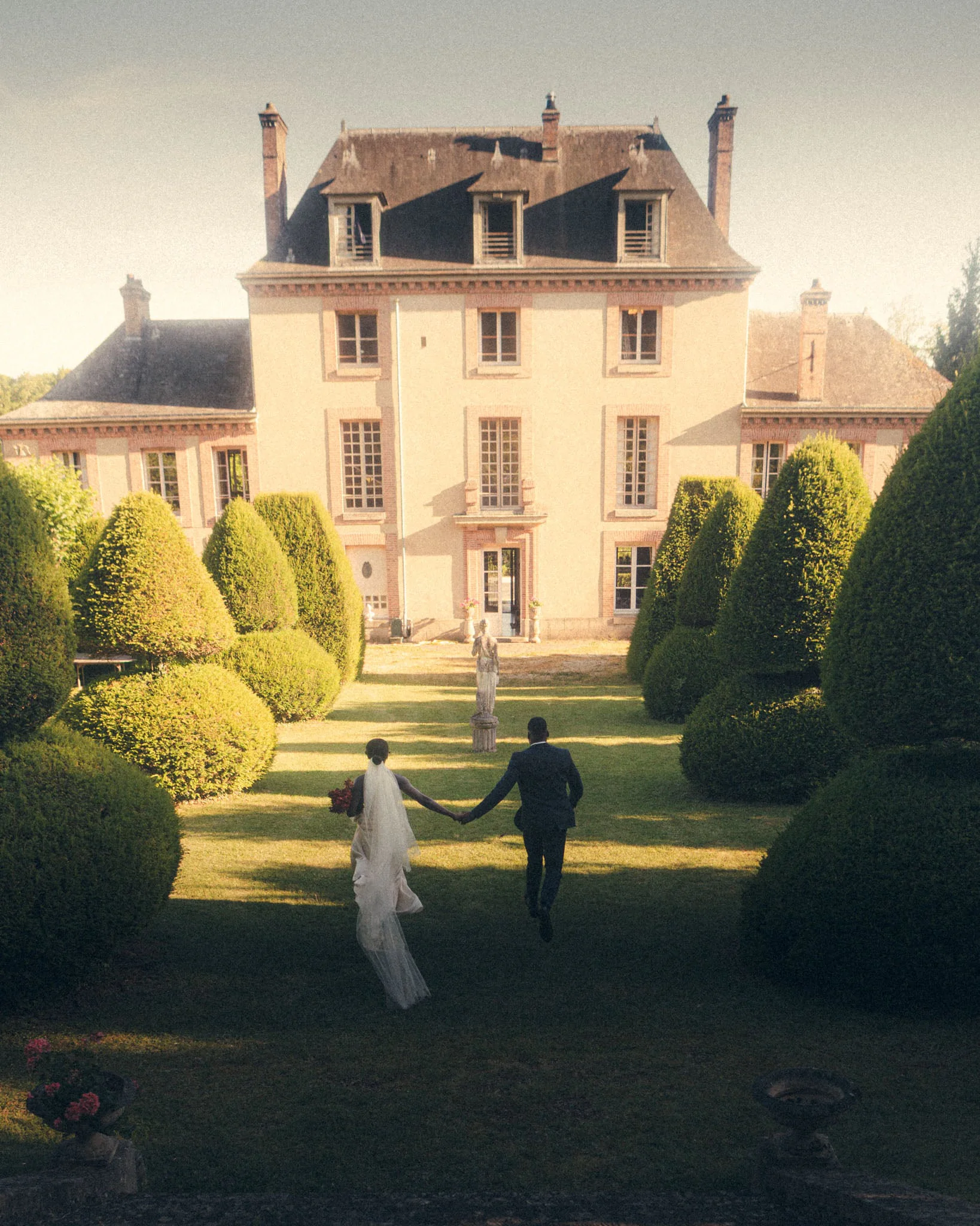Couple walking hand in hand across the lawn of a grand French chateau