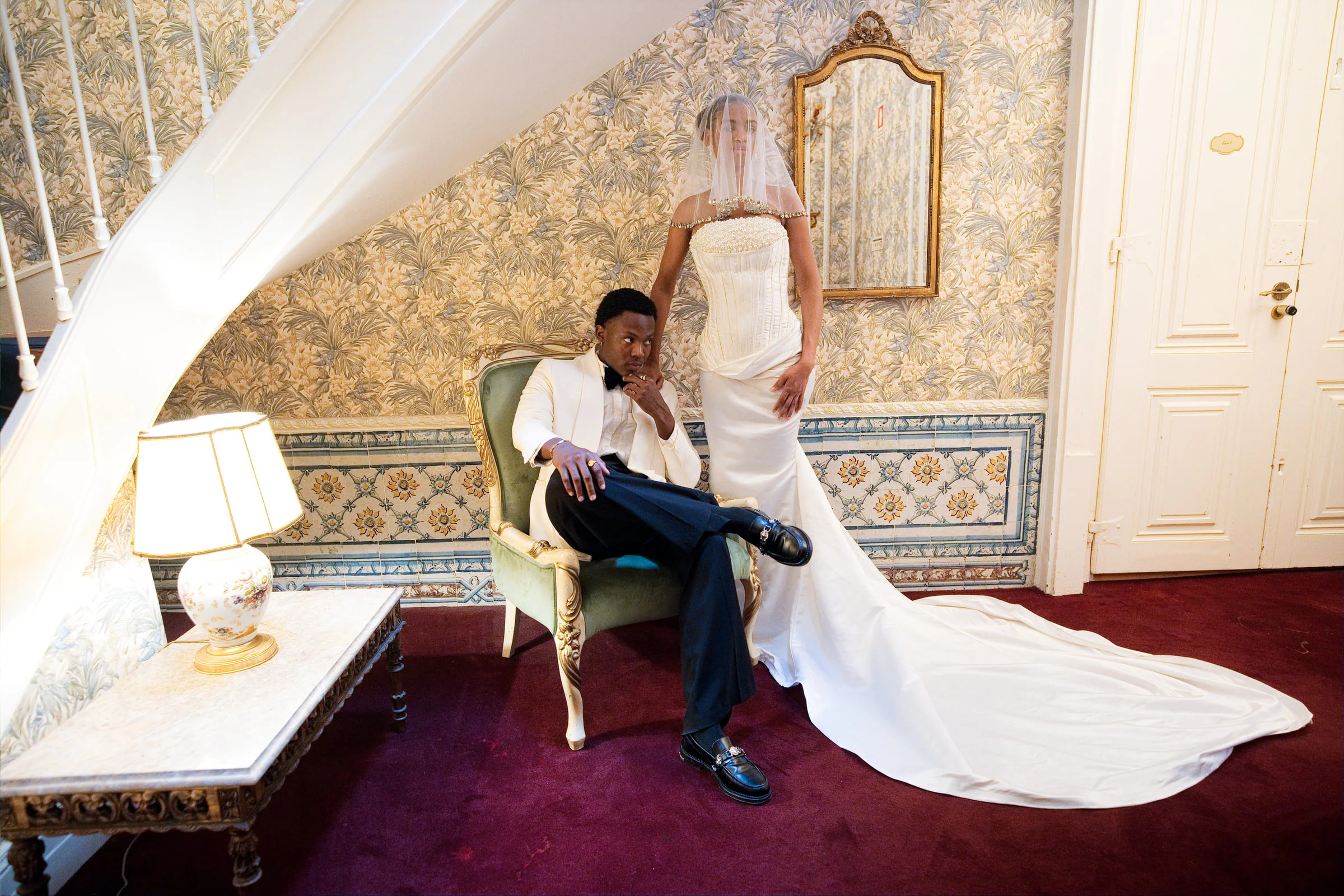 Bride in a sculptural corset gown standing behind her groom in a gilded armchair