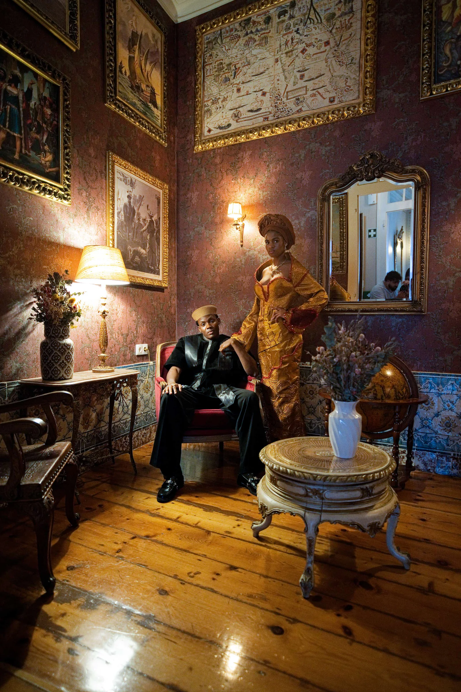 Couple seated in an ornate wood-panelled room lined with gilt-framed paintings