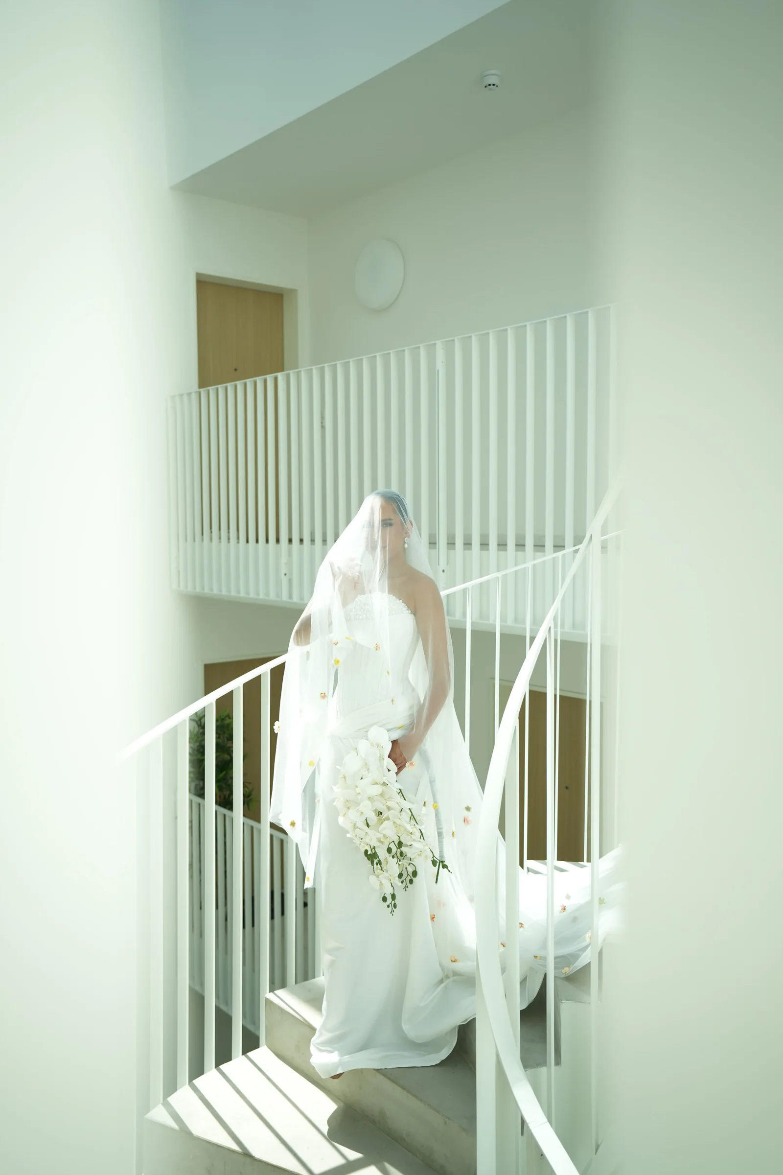 Bride in motion on a white architectural staircase, veil trailing behind her
