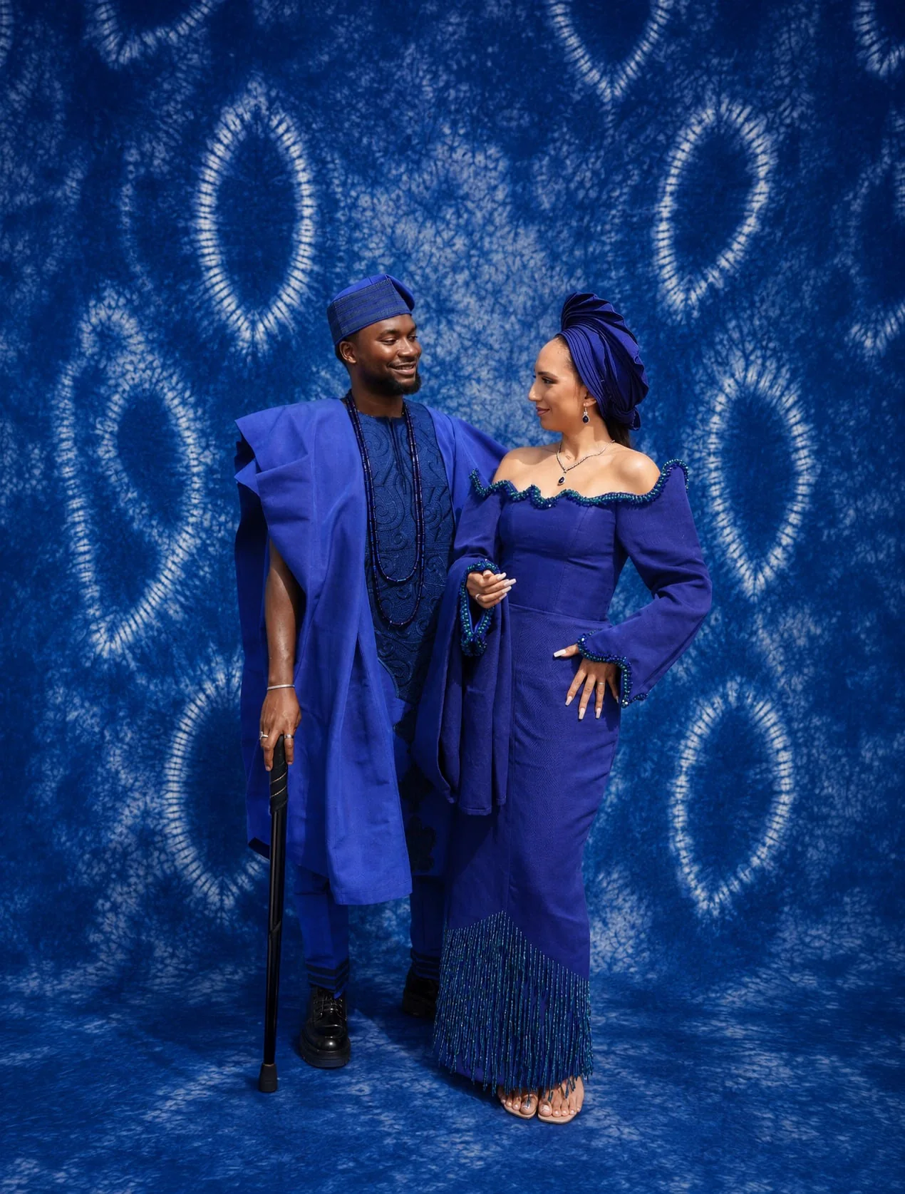 Couple in blue traditional attire posing against a tie-dye backdrop