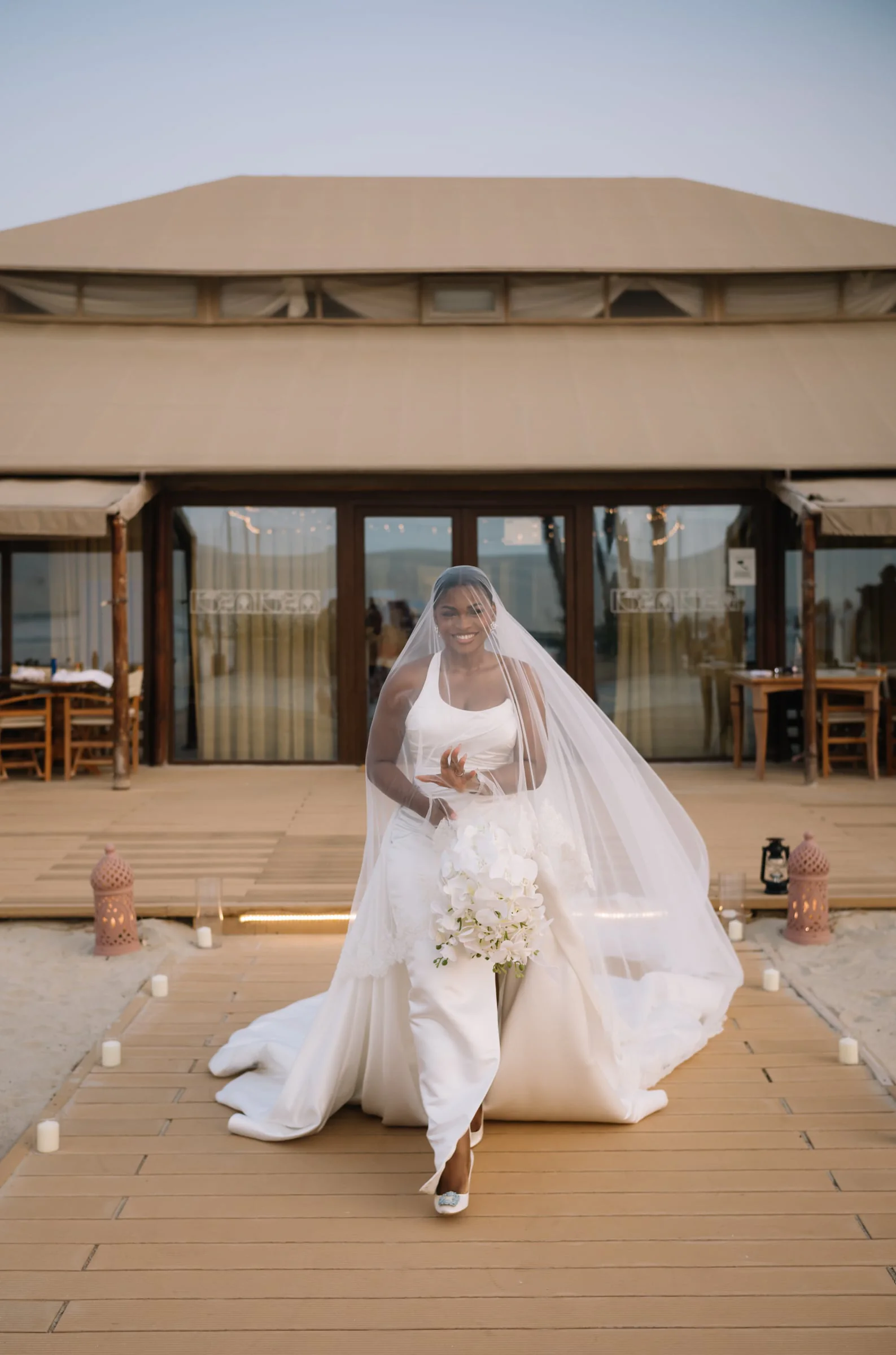 Bride walking a lantern-lined boardwalk toward the reception pavilion