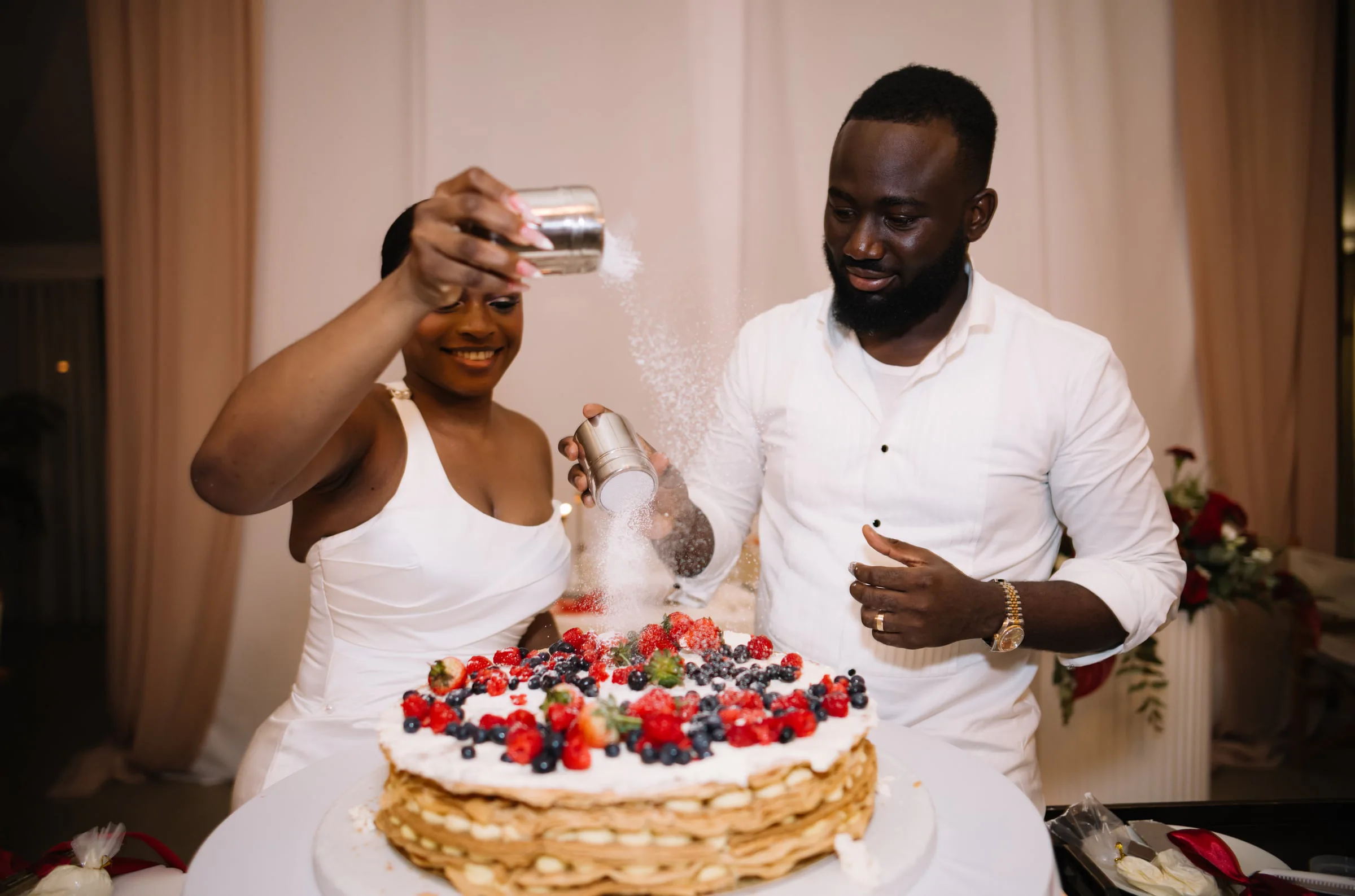 Bride and groom dusting powdered sugar over their berry wedding cake