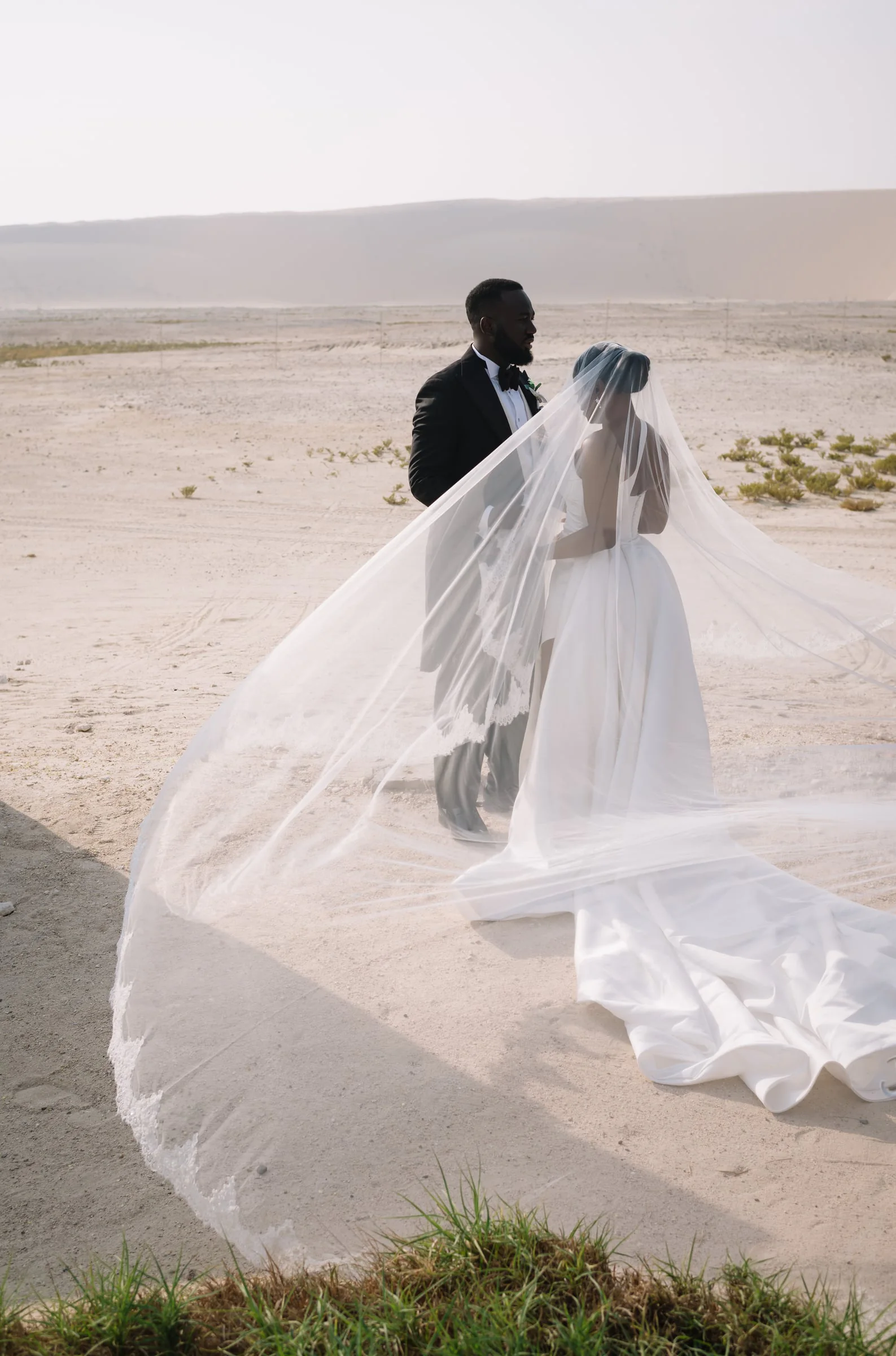 Bride’s cathedral veil billowing in the desert wind beside her groom