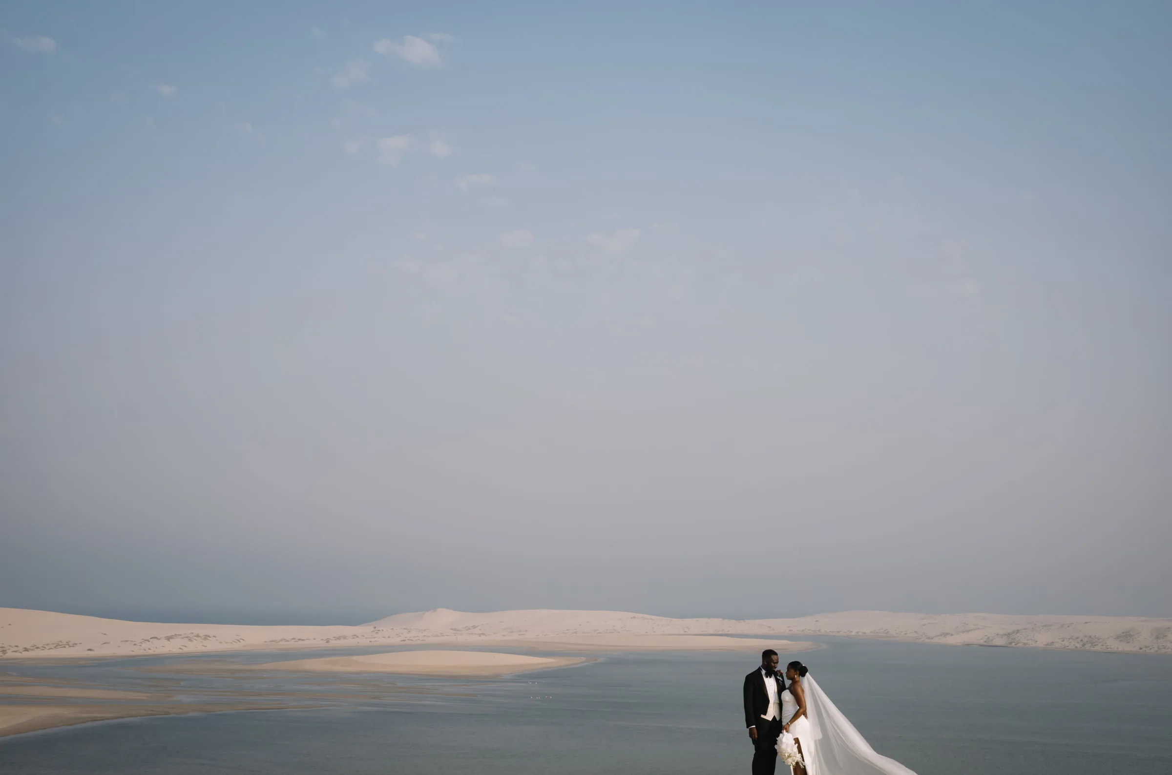 Couple standing atop sand dunes overlooking a desert lagoon